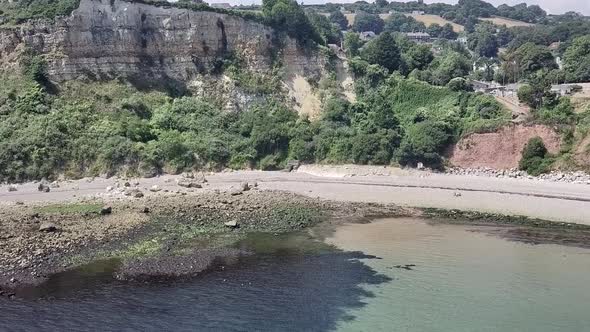 Flying while zooming in to beach in Seaton, England. Algae and rocks are visible in the water. The w