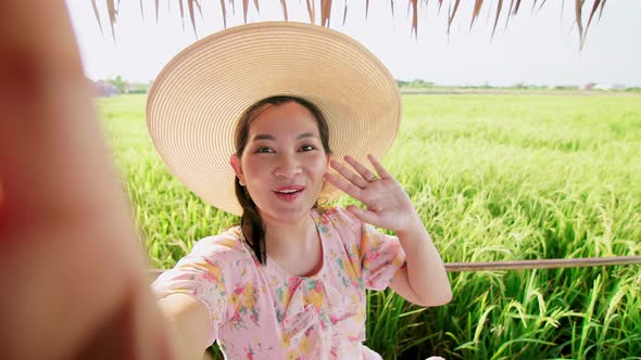 Adult woman making video call showing large rice production field.