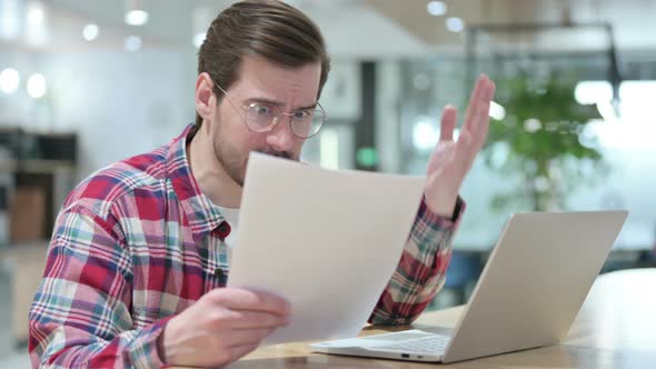 Angry Male Designer with Laptop Reacting To Loss on Documents 