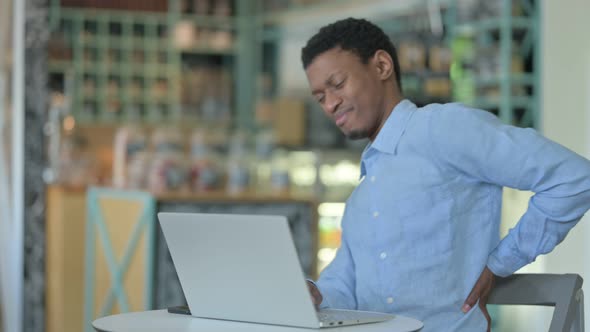 Young African Man with Back Pain Using Laptop in Cafe 