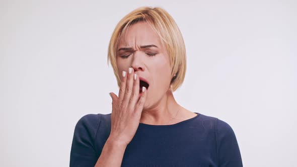 Sleepy Caucasian Middleaged Blonde Female in Blue Sweatshirt Yawning on White Background in