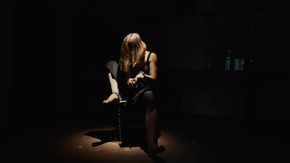 Woman Chained Sitting on a Chair in a Dark Creepy Room