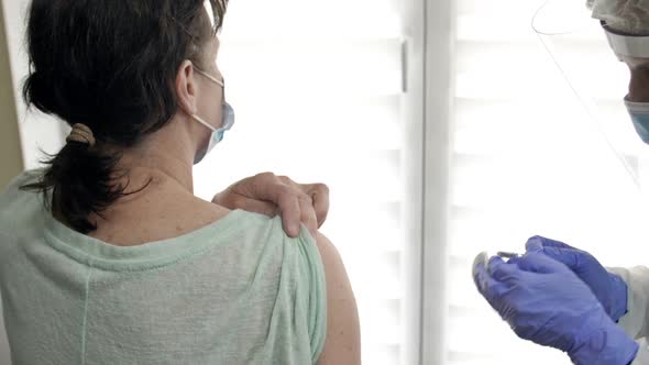 Doctor or Nurse Injects the COVID19 Vaccine Into an Elderly Female Patient's Shoulder