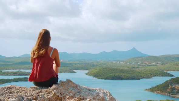 SLOWMO, Young woman sitting on rock high above Caribbean bay as wind blows hair