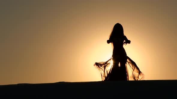 Girl with a Veil in Her Hands Dancing Belly Dance on the Beach. Silhouette