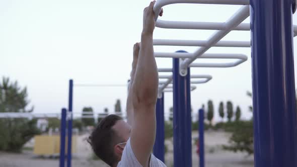 The athlete performs exercises on the horizontal bar in a medical mask.