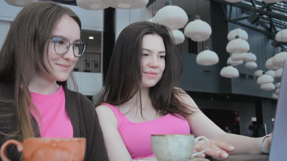 Two Girlfriends Sit in a Cafe and Look at Pictures