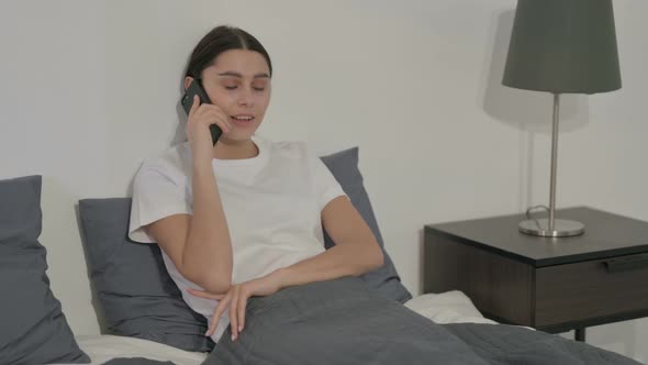 Hispanic Woman Talking on Call on Smartphone in Bed