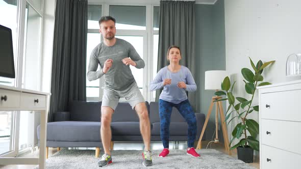 Caucasian Couple is Doing Squats and Kicks at Home in Cozy Bright Room Slow Motion