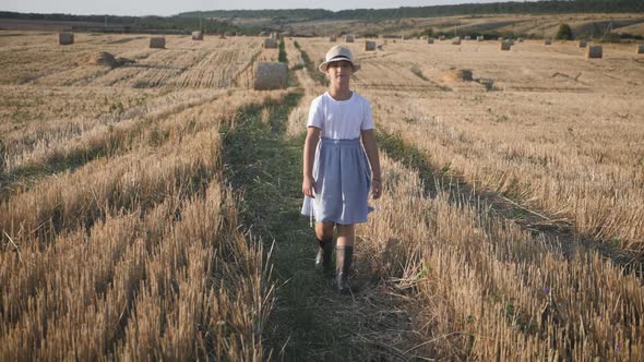 Pretty Girl in Blue Dress Walks in a Field with Haystacks.