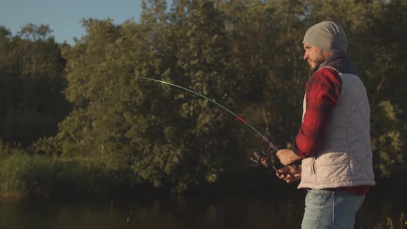 Fisherman with a spinning rod catching fish on a river.