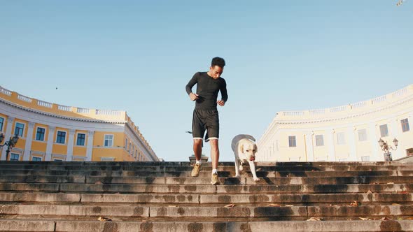 Young Black Man Running with His White Labrador Dog Down the Stairs in Old City Center During