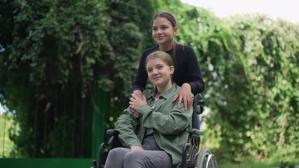 Portrait of Happy Disabled Girl in Wheelchair Looking at Camera Smiling Resting with Friend in