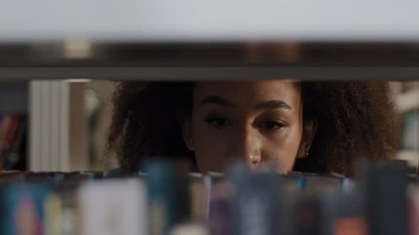 Young African American Girl Student Carefully Looking for Suitable Book on Bookshelf Concentrating