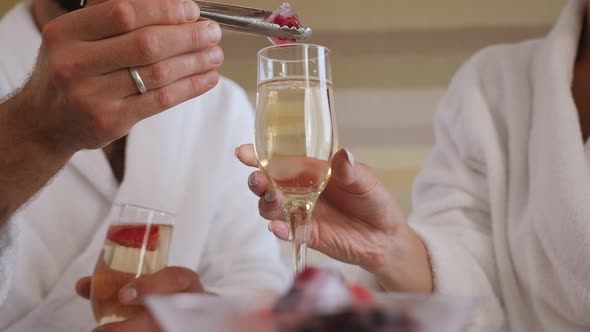 Closeup of a Man with Tongs Puts Ice with Berries in a Glass of Champagne