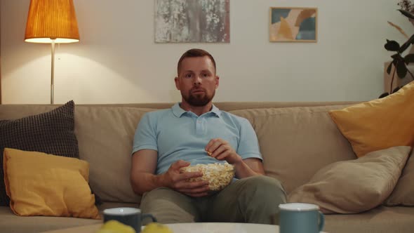 Scared Man Eating Popcorn while Watching Thriller on TV at Home