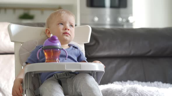 Cute Kid with Baby Straw Feeding Cup Sitting in Booster Seat One Year Old Toddler Watching Tv