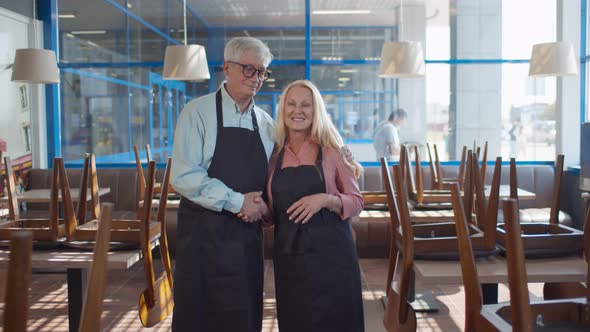 Two Senior Cheerful Owners of Contemporary Restaurant or Cafe Smiling at Camera