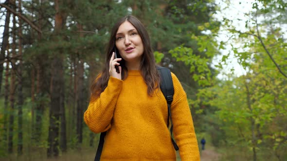 Hiker with Backpack Talks on Smartphone Walking Along Forest