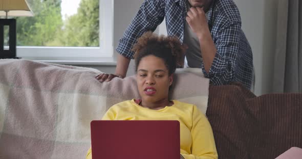 Portrait of Dissatisfied African American Woman Sitting on Couch Talking with Unrecognizable Man