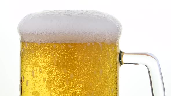 Pouring lager beer with bubbles and froth over the top in glass mug over white background