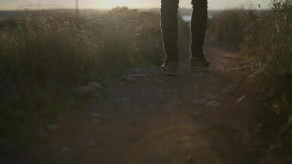 Legs of the Man Walking on a Countryside Trail Holding Guitar at Sunset  Slowmotion Following Shot