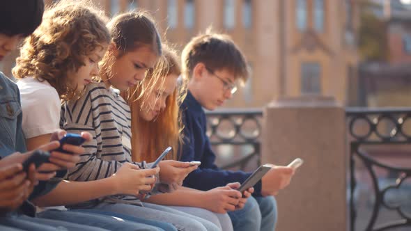 Group of School Children Sitting on Bench Outdoors Using Tablet Pc and Mobile Phone