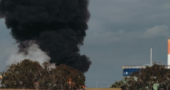 Accident in oil refinery - huge explosions and fireballs rising. Thick black smoke covers the sky.