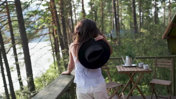 Young Woman in Shorts, a T-shirt and a Black Hat Enjoys Nature on a Terrace with Mountain Views