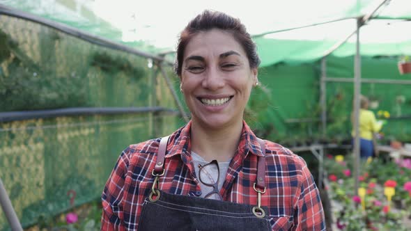 Happy Hispanic woman gardener smiling front of camera while working in flower garden shop