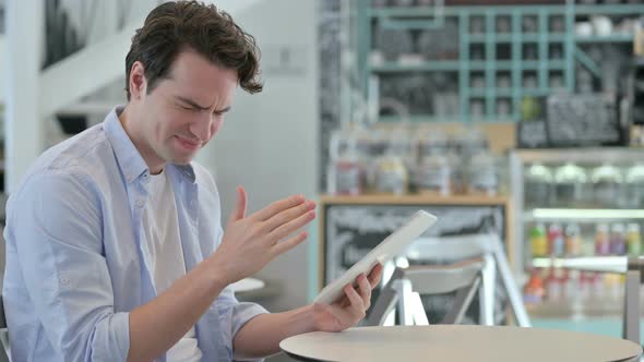 Young Man Reacting to Loss on Tablet in Cafe