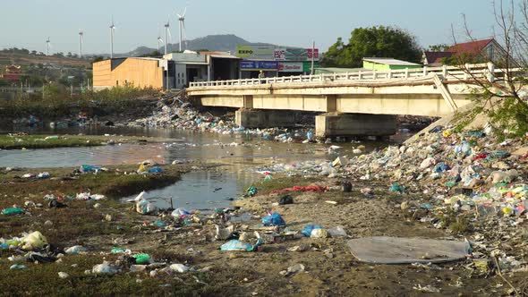 A bridge over a river polluted with plastic trash. Tons of plastic garbage are lying along the river