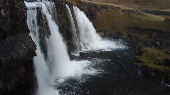 Flying near Kirkjufellsfoss Waterfall in west Iceland. Aerial shot of water cascades.