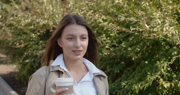 Young Attractive Business Woman Walks Around Historic Green Urban Area, with Take Away Cup and Drink