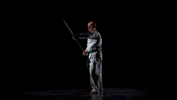 Kendo Fighter on White Kimono Practicing Martial Art with the Bamboo Bokken on Black Background