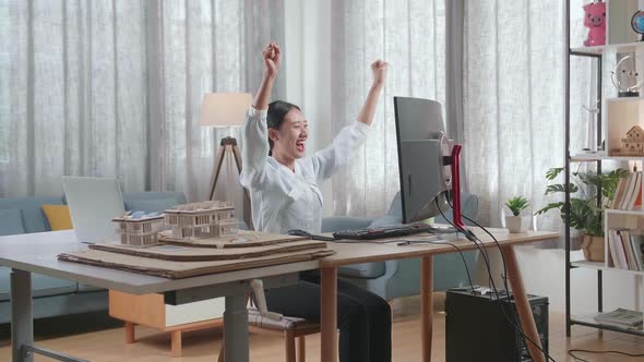 Asian Woman Engineer With The House Model Celebrating While Working On A Desktop At Home