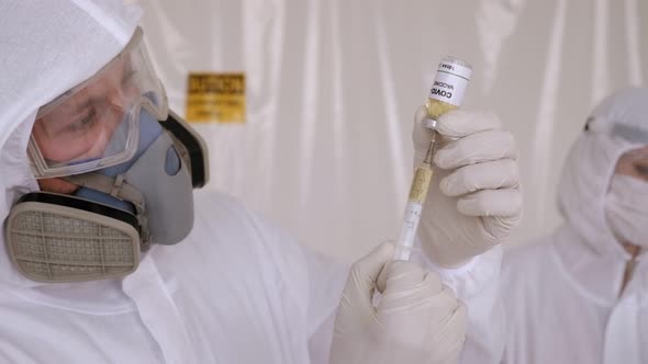 A Doctor in a Medical Suit Holding a Coronavirus Vaccine and a Syringe