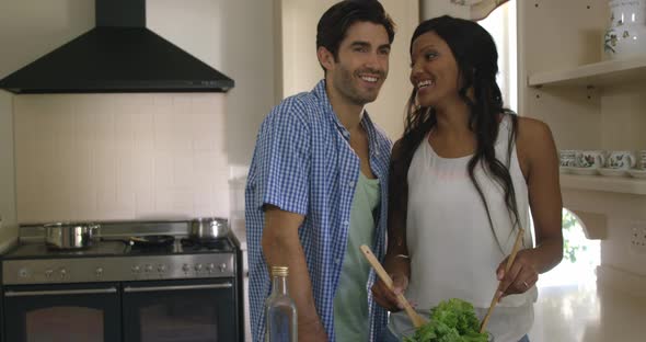 Man kissing a woman while mixing a salad in kitchen