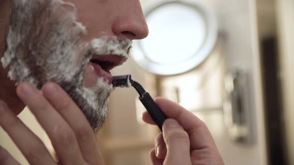 Men Face Hair Care. Male Shaving Beard With Razor Closeup