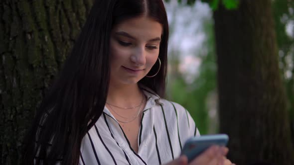 Woman Using Mobile Phone Resting in Park Sitting Under Tree