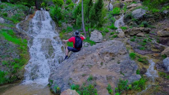 Man is Sitting on a Stone and Raising His Hands Up