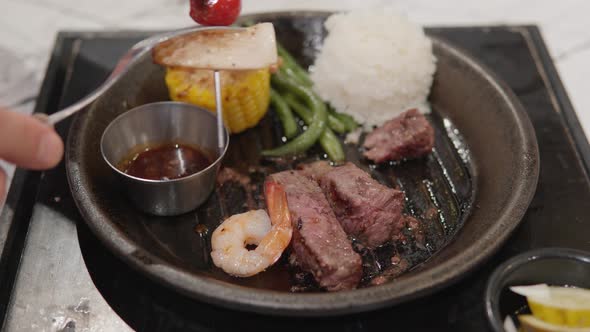 Removing Shrimp And Vegetables From Skewer To Sizzling Plate With Beef Steak And Rice. close up