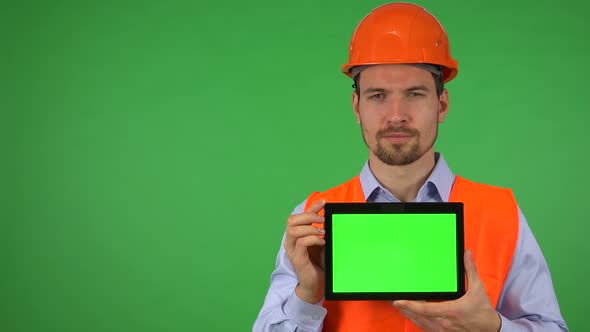 A Young Construction Worker Shows a Tablet with Green Screen To the Camera - Green Screen Studio