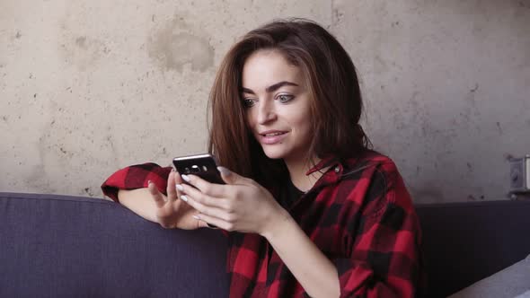 Young Beautiful Brunette Girl Looks at Her Smartphone and Acts Surprised