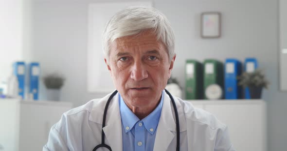 Serious Mature Doctor Wearing White Uniform Coat with Stethoscope Speaking Looking at Camera