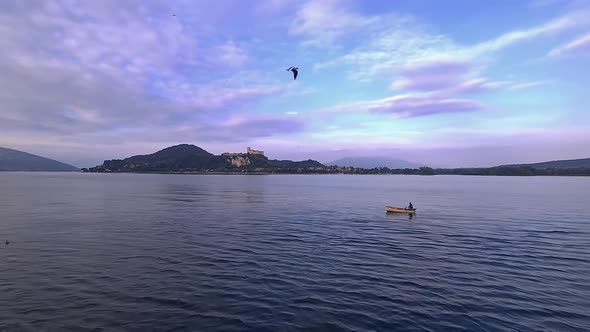 Wide-angle pov of small fishing boat with fisherman rowing in calm lake waters of Maggiore lake in I