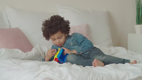 Serious Cute Little Kid Repairing Toy Car on Bed