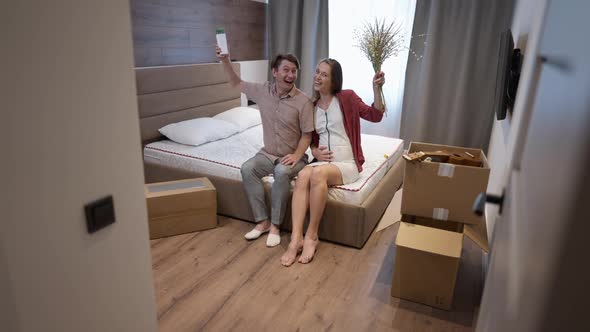 Wide Shot Happy Couple Sitting on Bed Smiling Showing Flowers Looking at Camera in Slow Motion