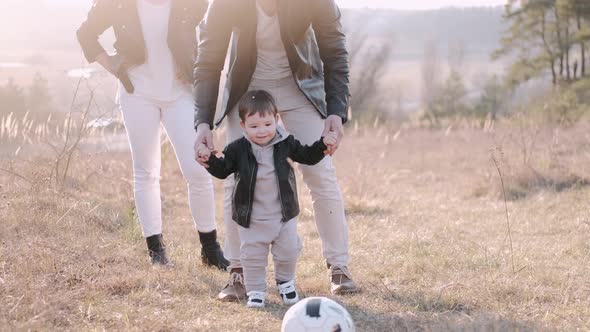 Happy Parents and a Cute Son Are Playing Football Outside