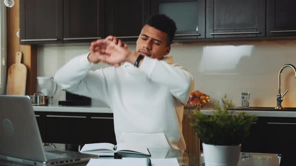 Tired Black Man Exercising While Working on the Computer in the Kitchen at Home